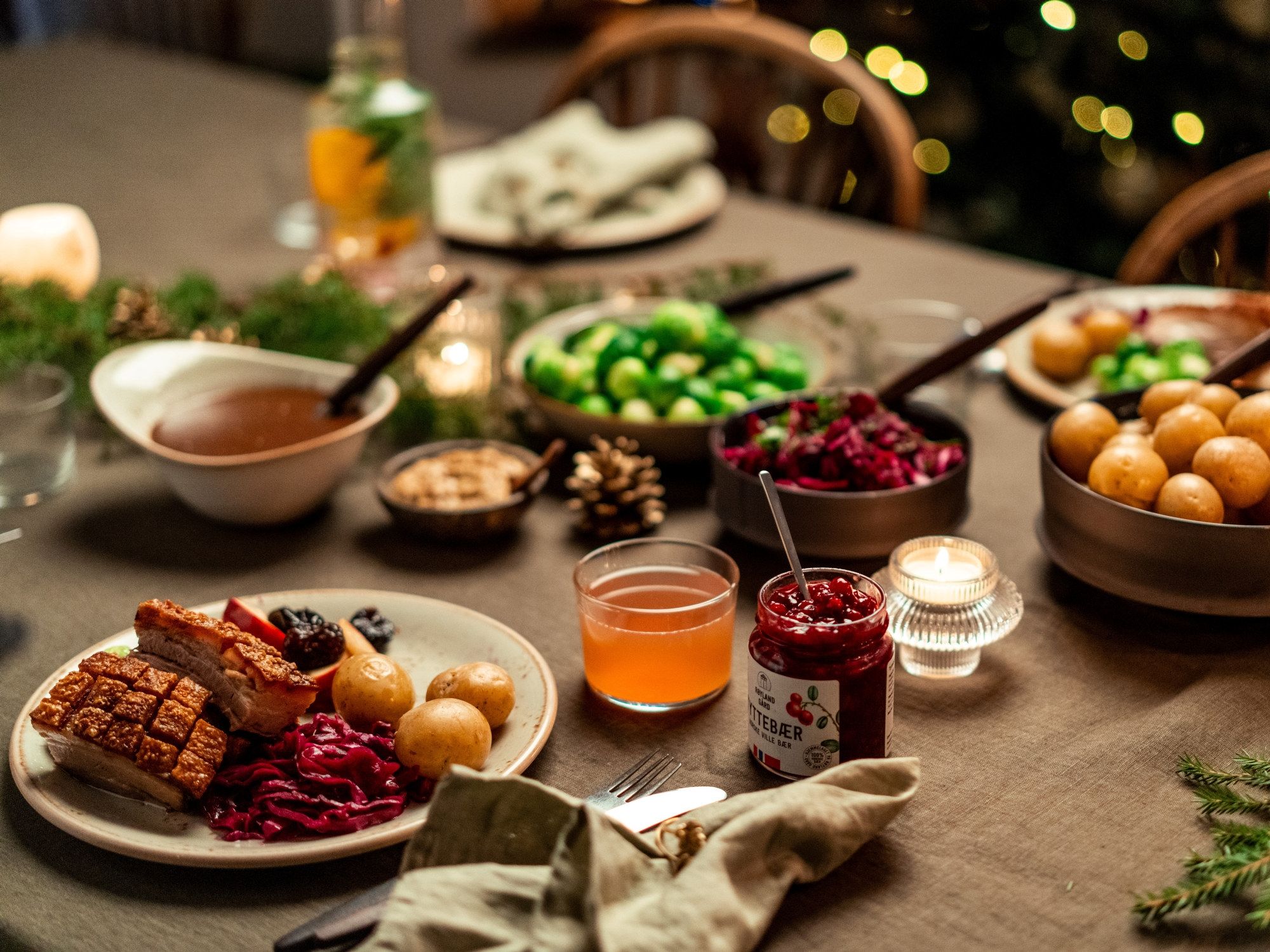 Et bord dekket med julemat og julegodt, inkludert kaker, syltetøy, frukt og nøtter, med julelys i bakgrunnen.