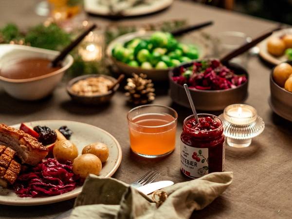 Et bord dekket med julemat og julegodt, inkludert kaker, syltetøy, frukt og nøtter, med julelys i bakgrunnen.