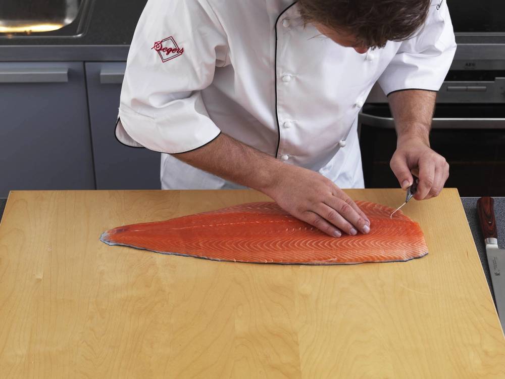 Person som fileterer en hel laksefilet på et kjøkkenbord.