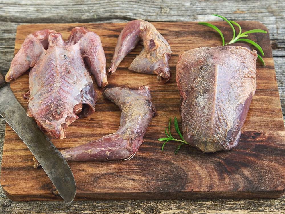 Ulike stykker av rått viltkjøtt på en skjærefjøl med en kniv og noen grønne urter.