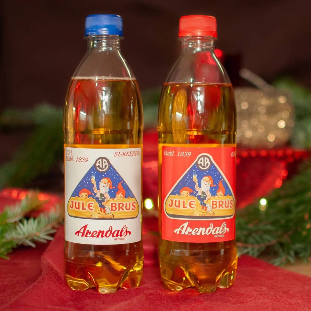To flasker med Arendals julebrus står på et bord med julepynt rundt, en med blå og en med rød korkhette.