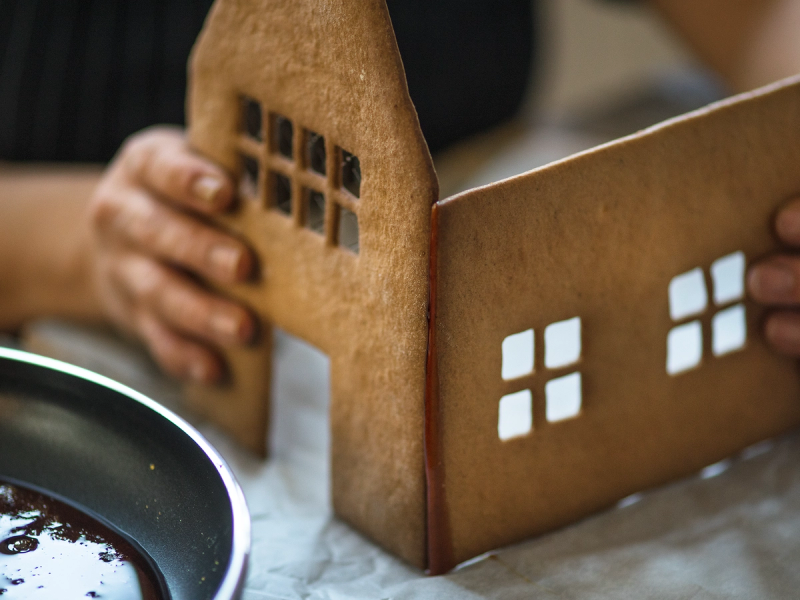 Person som bygger et pepperkakehus med vindusdetaljer av pepperkaker.