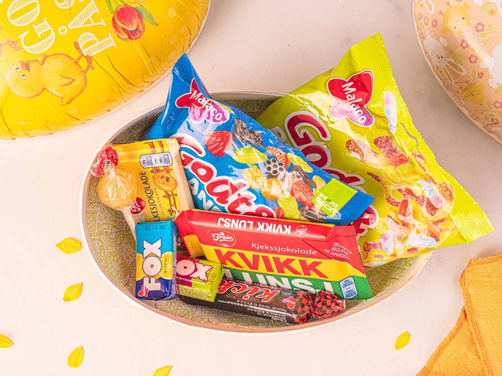Smågodt i en skål med ulike godterier og godteriposer rundt på et bord, sannsynligvis til fest eller kos.