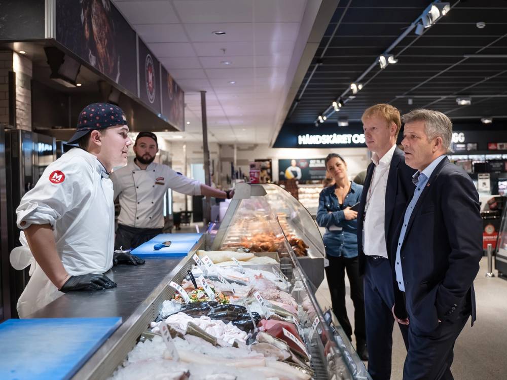 Fiskeriminister deltar i en samtale med ansatte i en fiskebutikk eller marked.