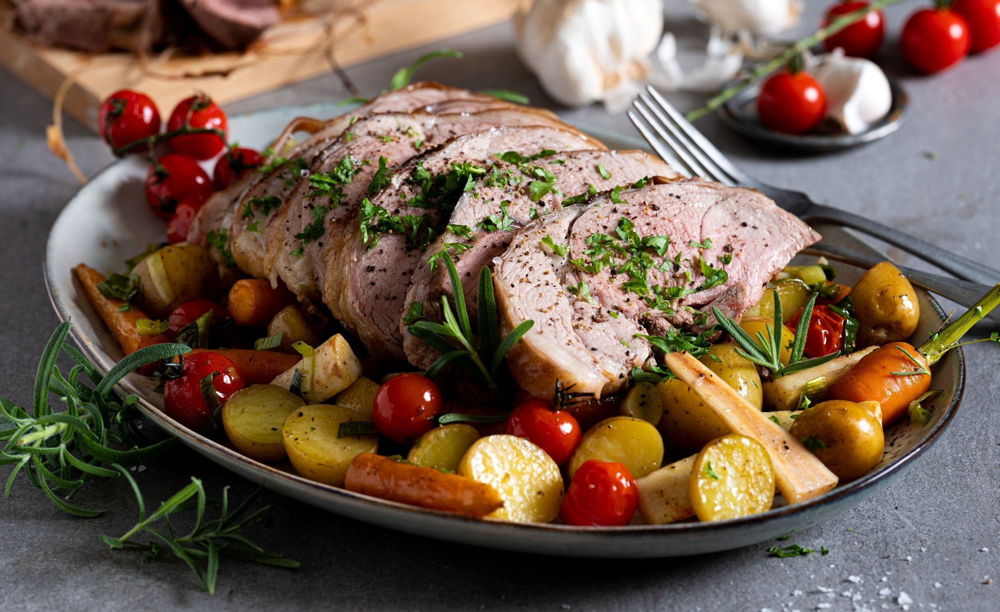 Lammestek med ovnsbakte grønnsaker og urter på et serveringsfat.