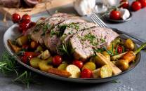 Lammestek med ovnsbakte grønnsaker og urter på et serveringsfat.