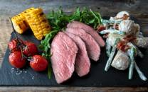 Servering av stekt biff med grillede maiskolber, cherrytomater, salat og potetsalat på en svart skjærefjøl.