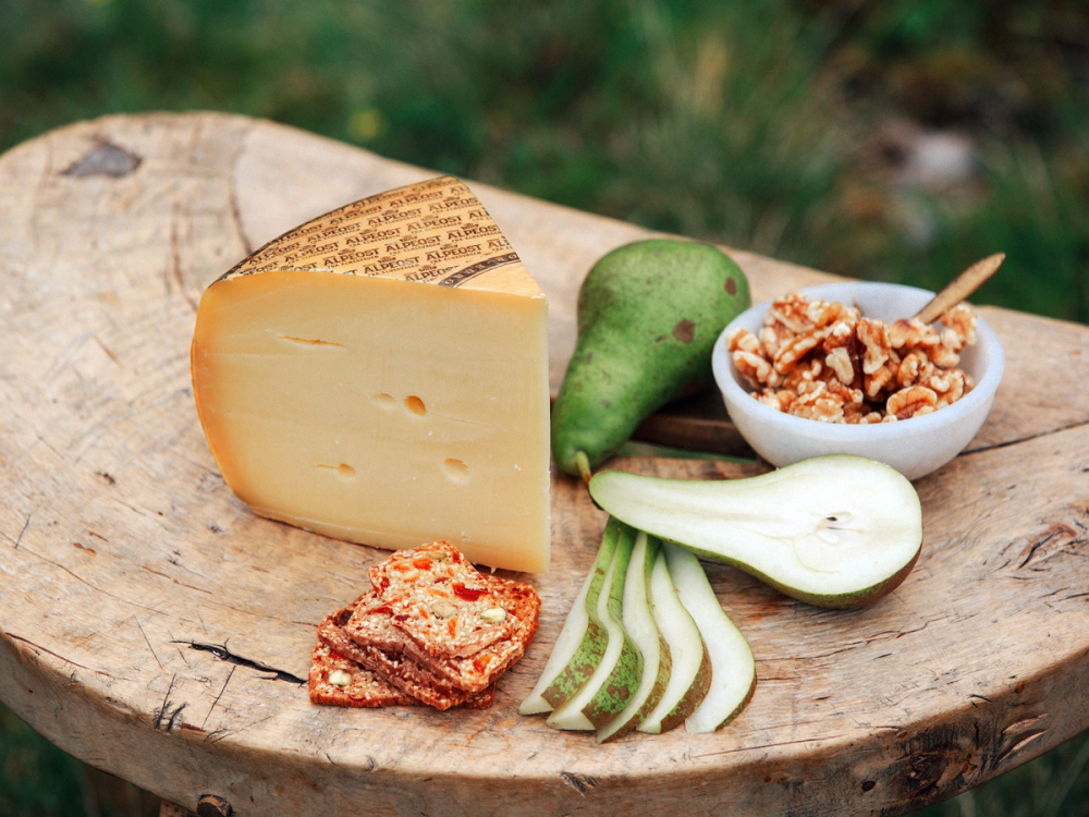 Skivet alpeost sammen med en pære, løk, nøtter og tørket frukt på et trestykke, som tilbehør.