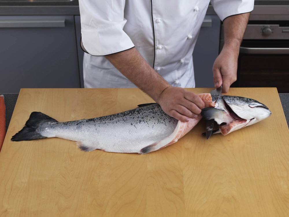 Person som fileterer en hel laks på et kjøkkenbord.