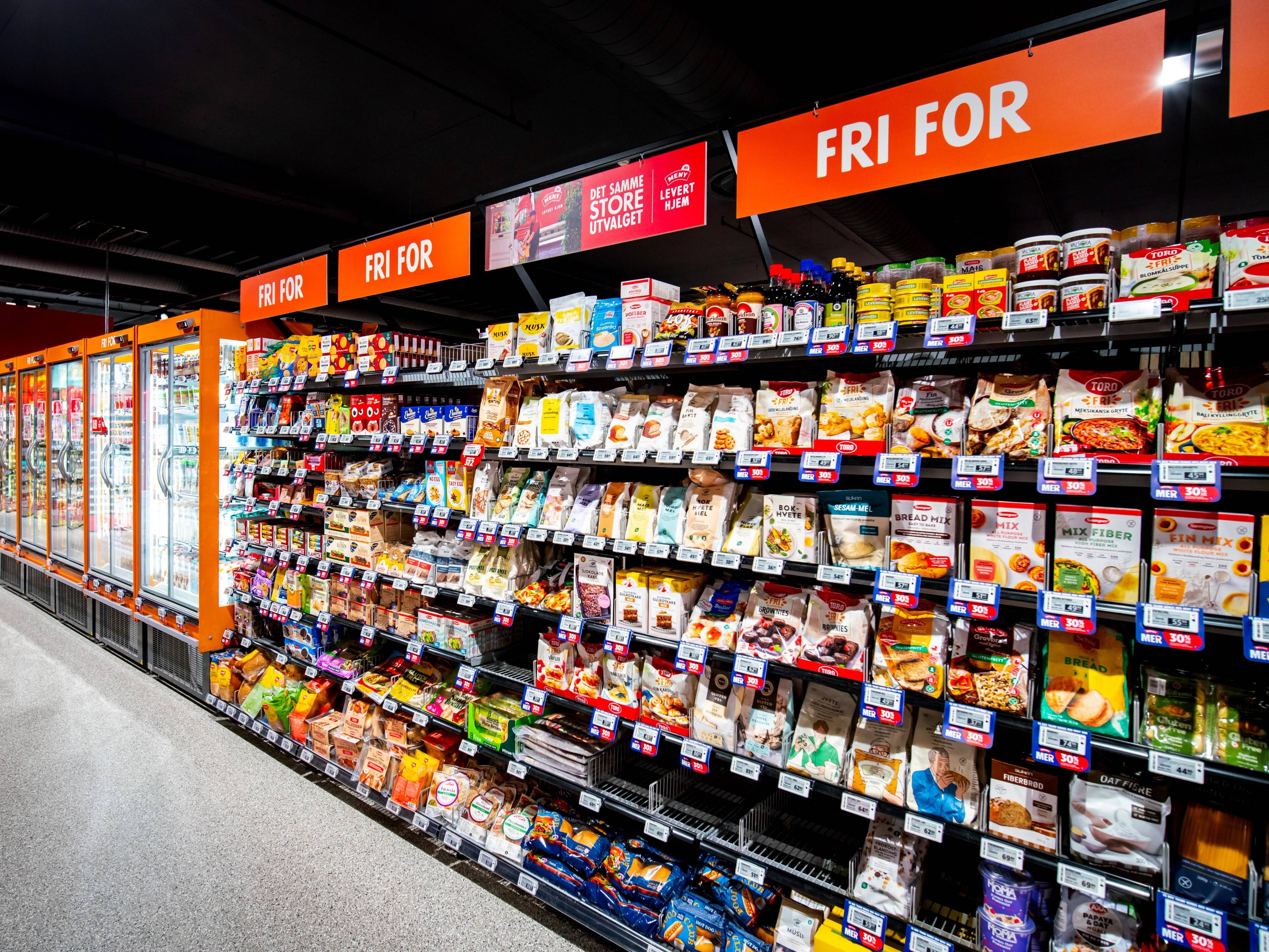 Hylla i en dagligvarebutikk med ulike matvarer og en stor skilt som sier 'FRI FOR' i bakgrunnen.