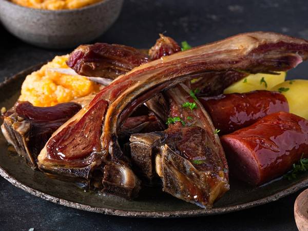 Pinnekjøtt med kålrotstappe og poteter på et svart fat.