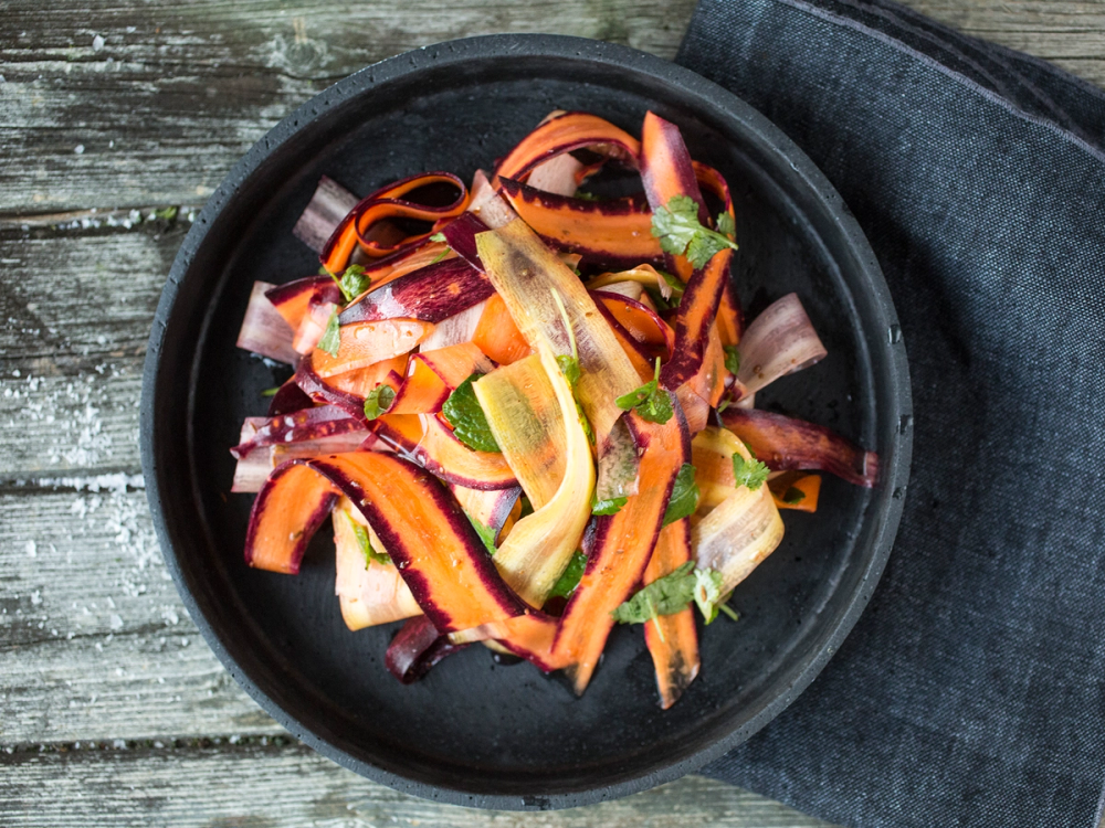 En skål med frisk gulrotsalat blandet med krydder og urter, ser fargerik og innbydende ut.