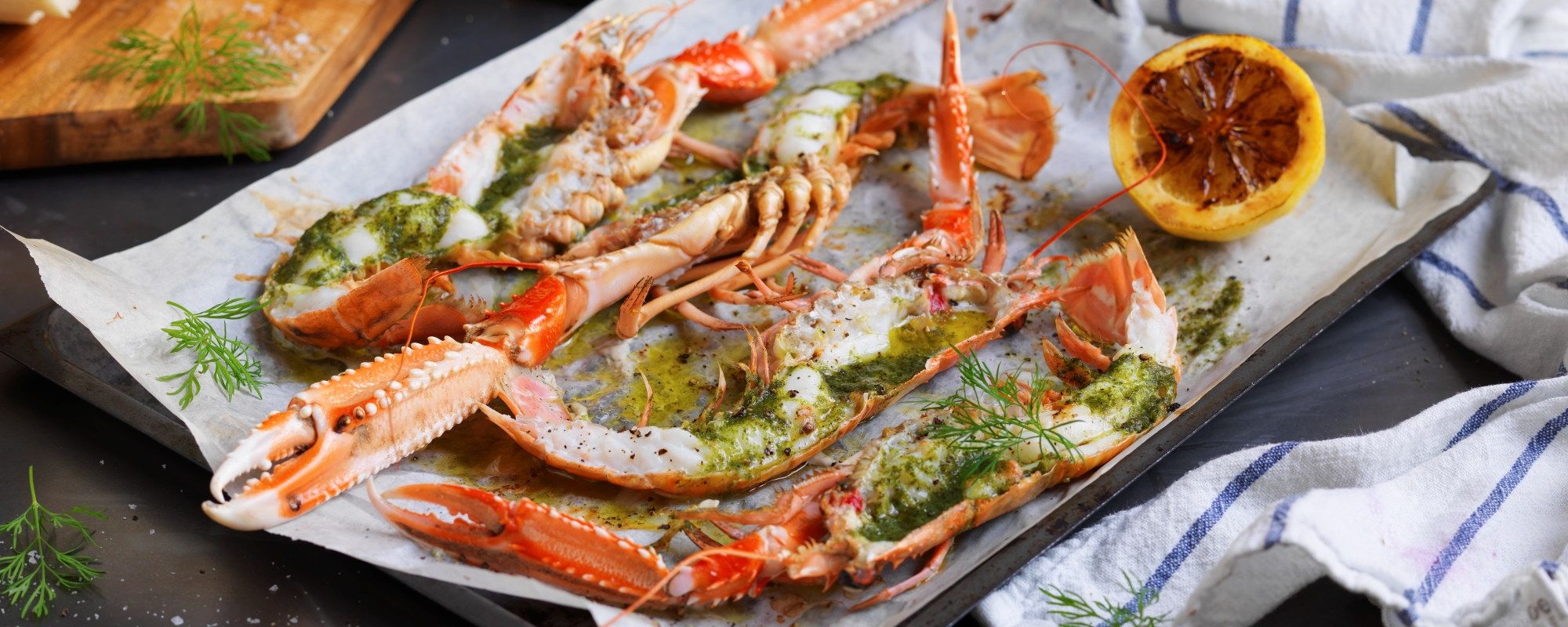 Gratinerte sjøkreps med ramsløksmør på et serveringsfat med sitronbåter ved siden av.