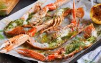 Gratinerte sjøkreps med ramsløksmør på et serveringsfat med sitronbåter ved siden av.