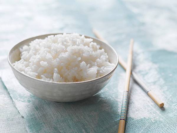 En skål med kokt sushiris på et bord med spisepinner ved siden av.