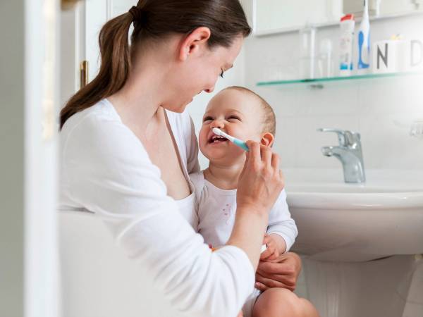 En voksen hjelper et barn med å pusse tennene på badet.
