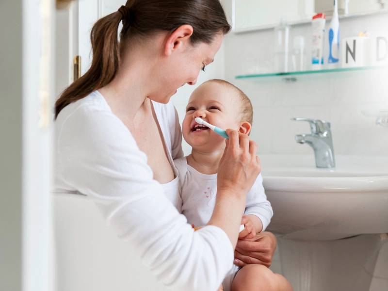 En voksen hjelper et barn med å pusse tennene på badet.