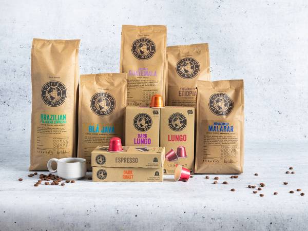 Ulike eske- og posepakker med kaffebønner og kaffekapsler på en hvit bakgrunn, med noen kaffebønner spredt rundt.