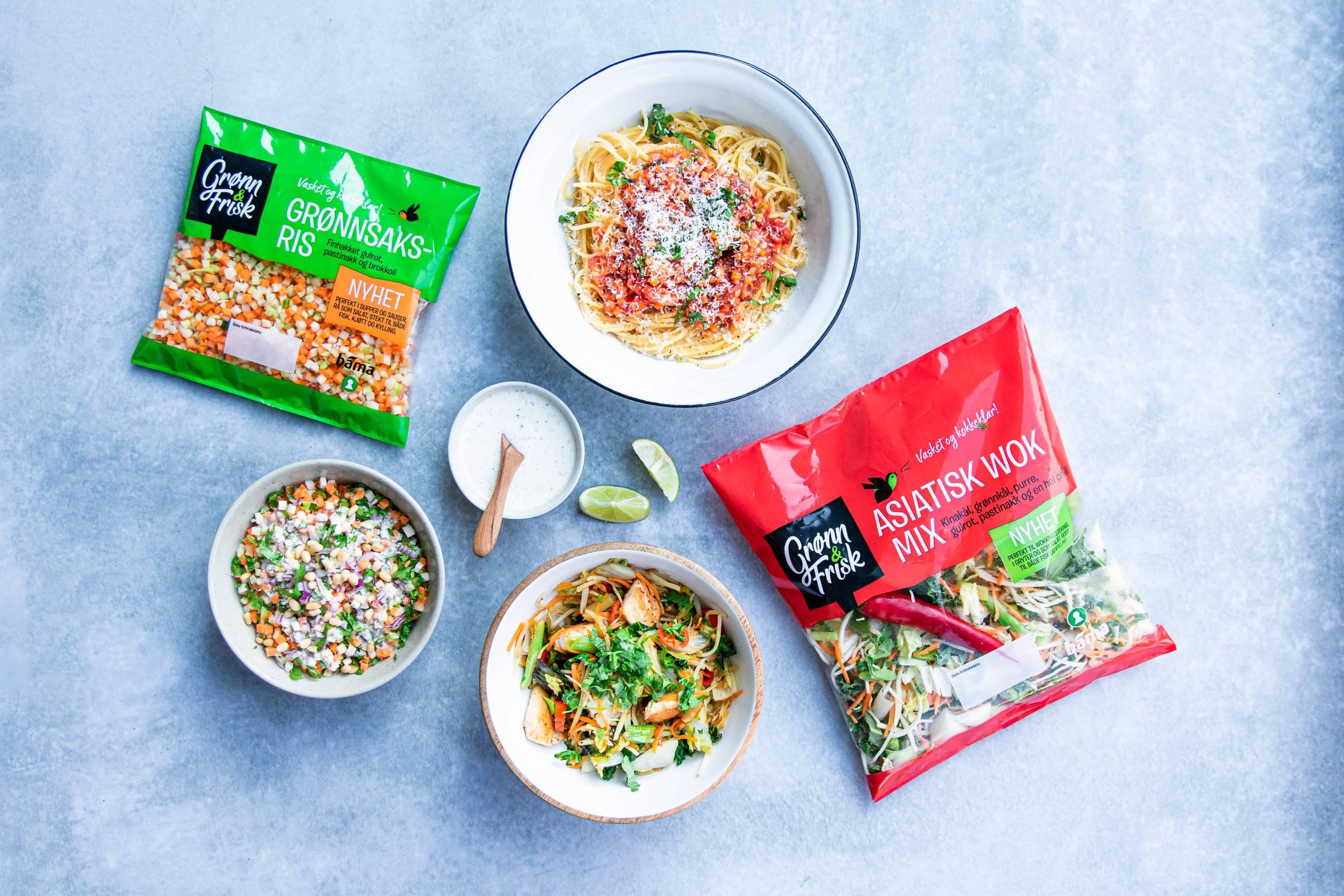 Pakke med grønnsaksris og to ferdige wok-retter i små boller, med en skje og limebåter på et lyst bord