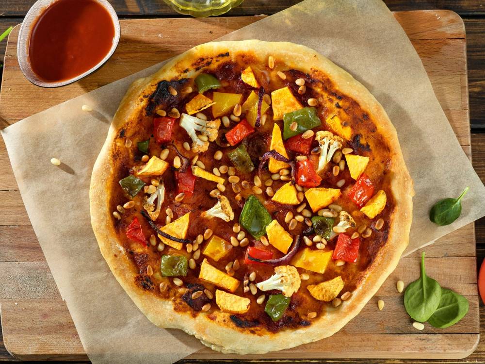 Vegansk pizza uten ost med paprika, løk og grønne urter på en treplate, med en liten skål med tomatsaus ved siden av.