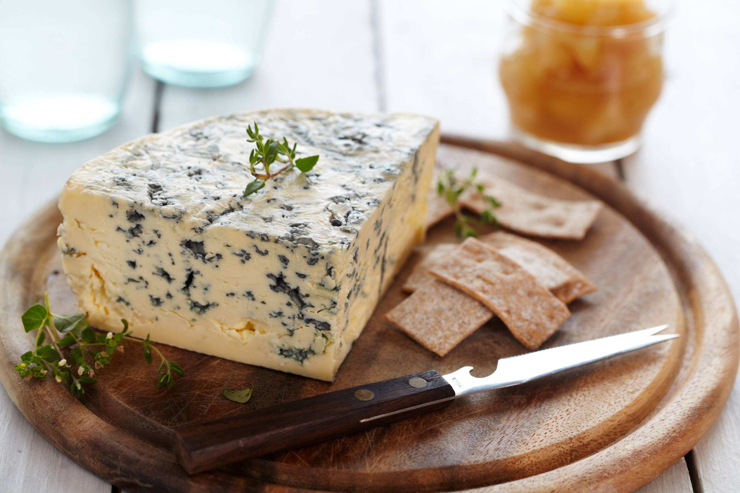 Blåmuggost på et rundt trefat med kjeks og urter, med et glass syltetøy i bakgrunnen.