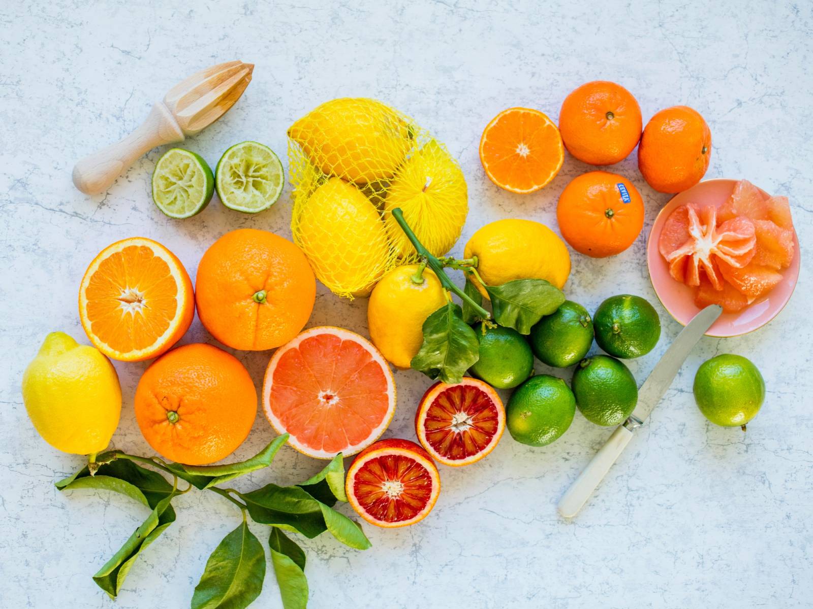 Fargerike sitrusfrukter som appelsiner, sitroner, lime, grapefrukt og klementiner ligger på en lys overflate.
