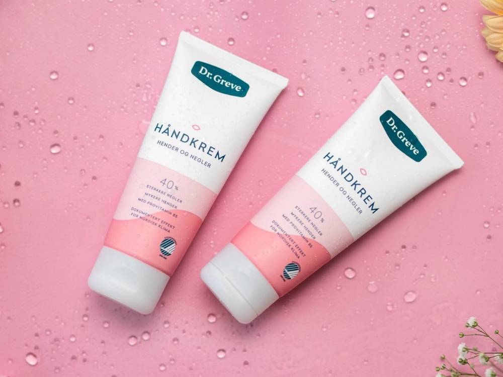 To tuber med Dr Greve håndkrem plassert på en rosa bakgrunn med vannperler rundt.