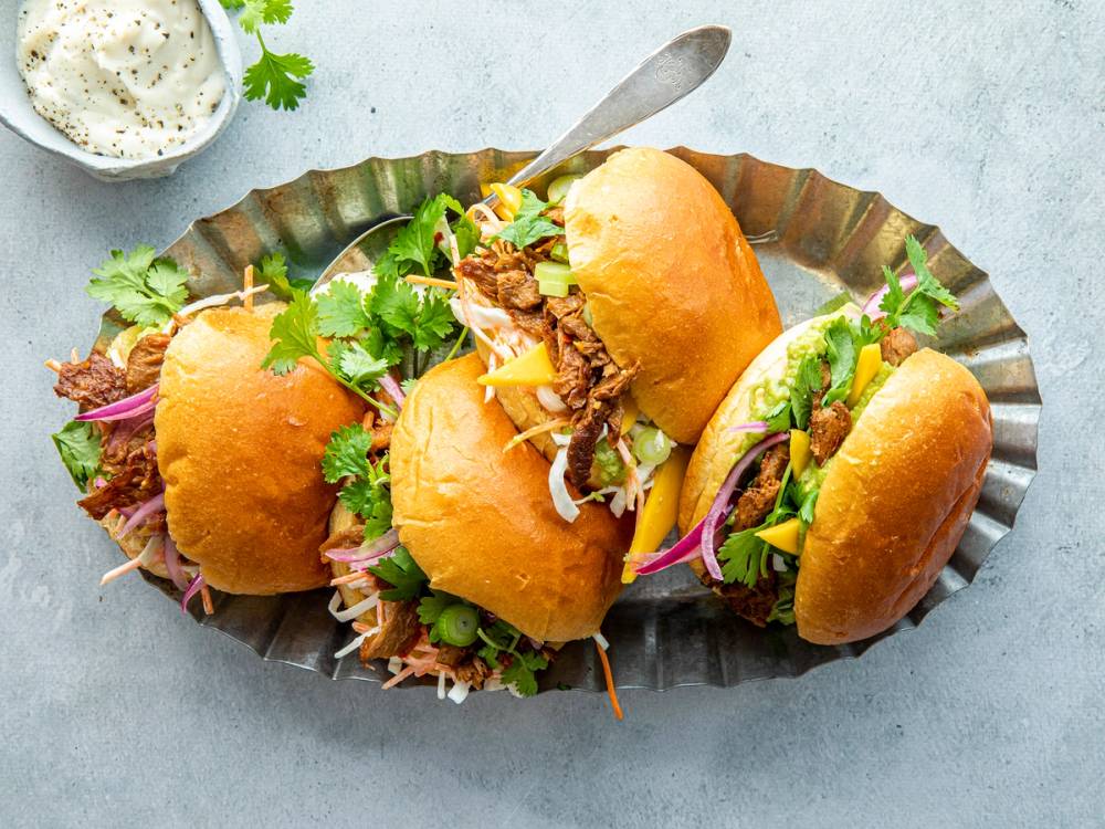 Tre veganske sliders med briochebrød fylt med plantebasert kjøttdeig og grønnsaker på et fat.