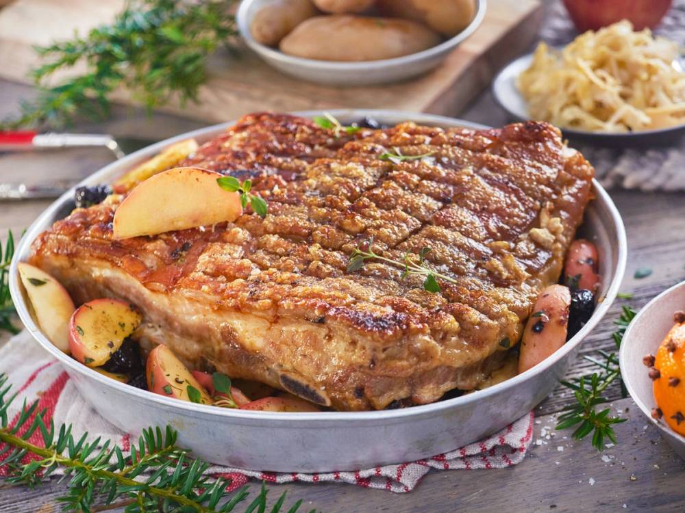 Stekt ribbe med sprø svor på et fat, omgitt av julekrydder og tilbehør som poteter og grønnsaker, klar til servering.