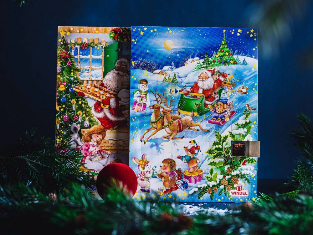 To kalendere med jule- og vintermotiver, plassert mot en blå bakgrunn med julepynt og granbar rundt.