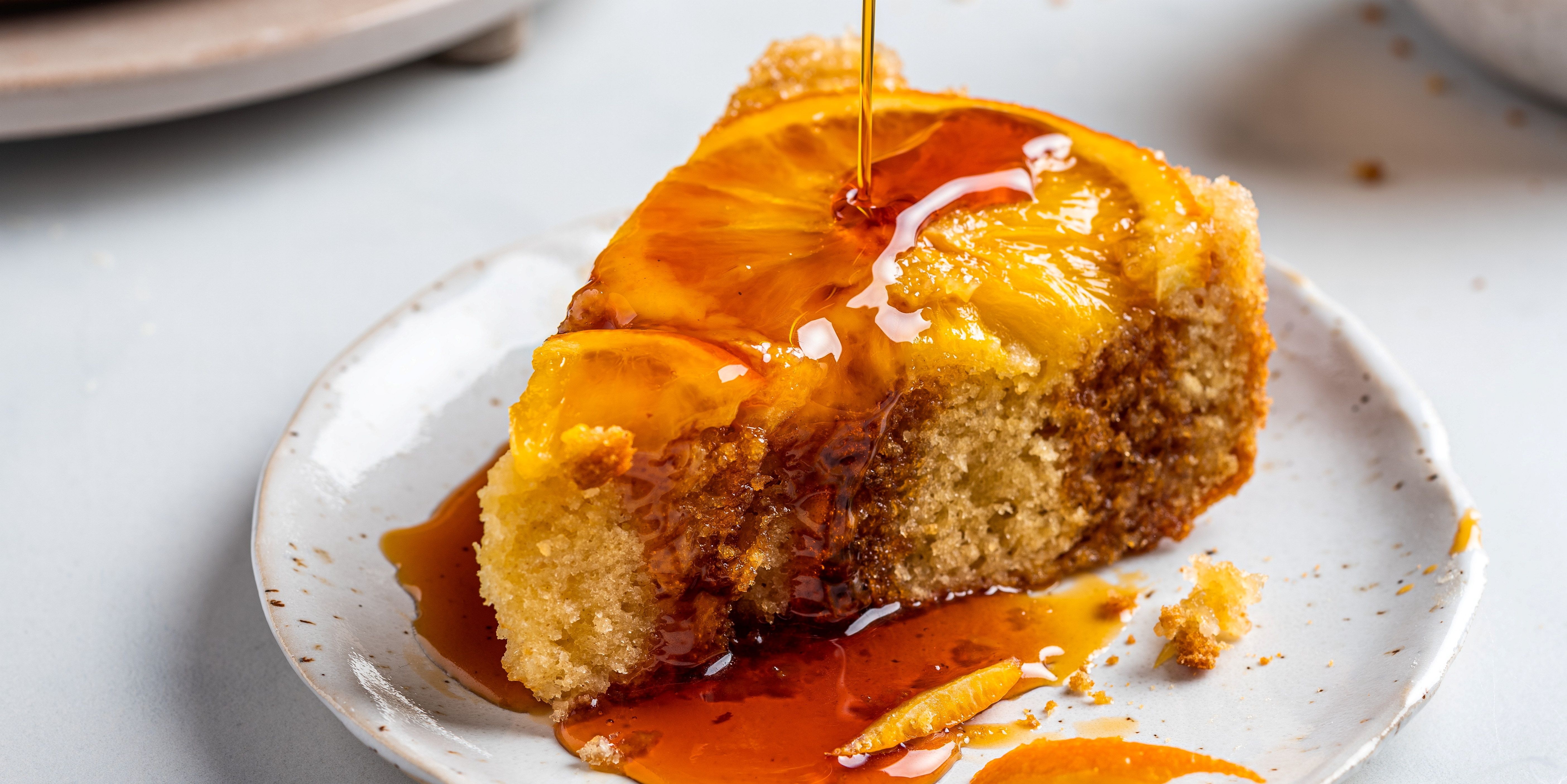 En opp ned appelsinkake med glasur som drypper ned på en hvit tallerken