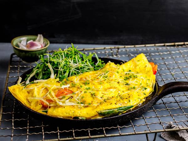 Stekt ris med omelett og grønnsaker på en svart grillrist, med en liten skål med salat ved siden av