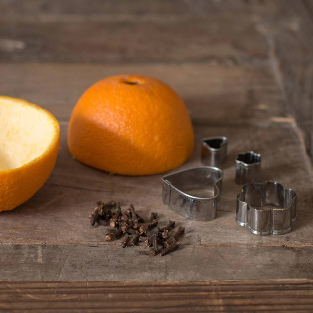 En hel klementin, en halvert klementin og noen krydderkuttere på et trebord.