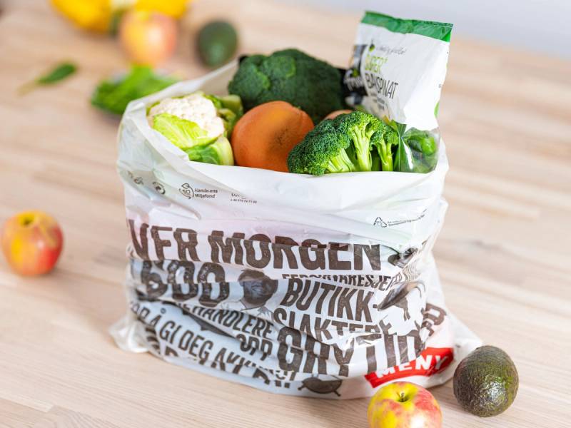 En plastpose fylt med ulike grønnsaker som brokkoli, gulrot og blomkål, plassert på et kjøkkenbord.