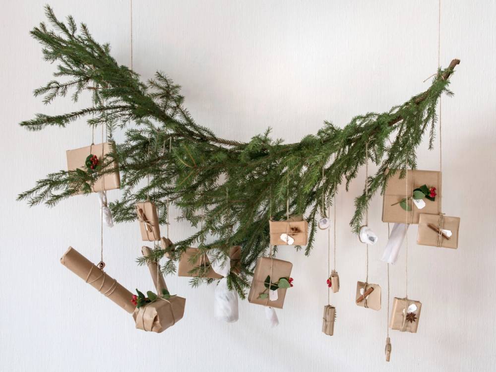 En dekorativ julegren med små gavepakker og julepynt hengende fra den, festet til en hvit vegg.