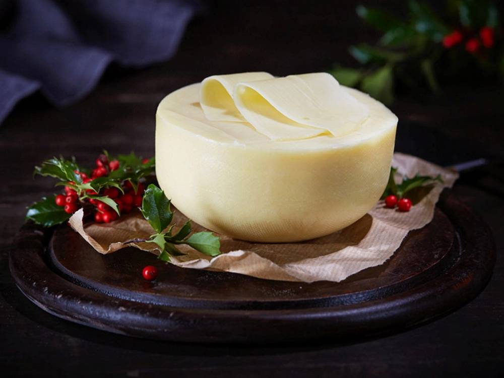 En blokk av hvit edamerost på et fat med julegrener og røde bær rundt, klar til servering.