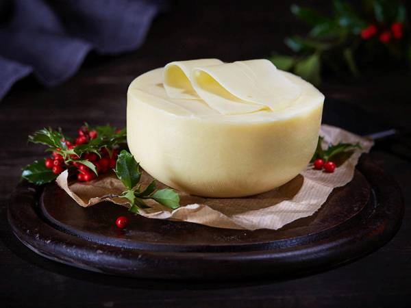 En blokk av hvit edamerost på et fat med julegrener og røde bær rundt, klar til servering.