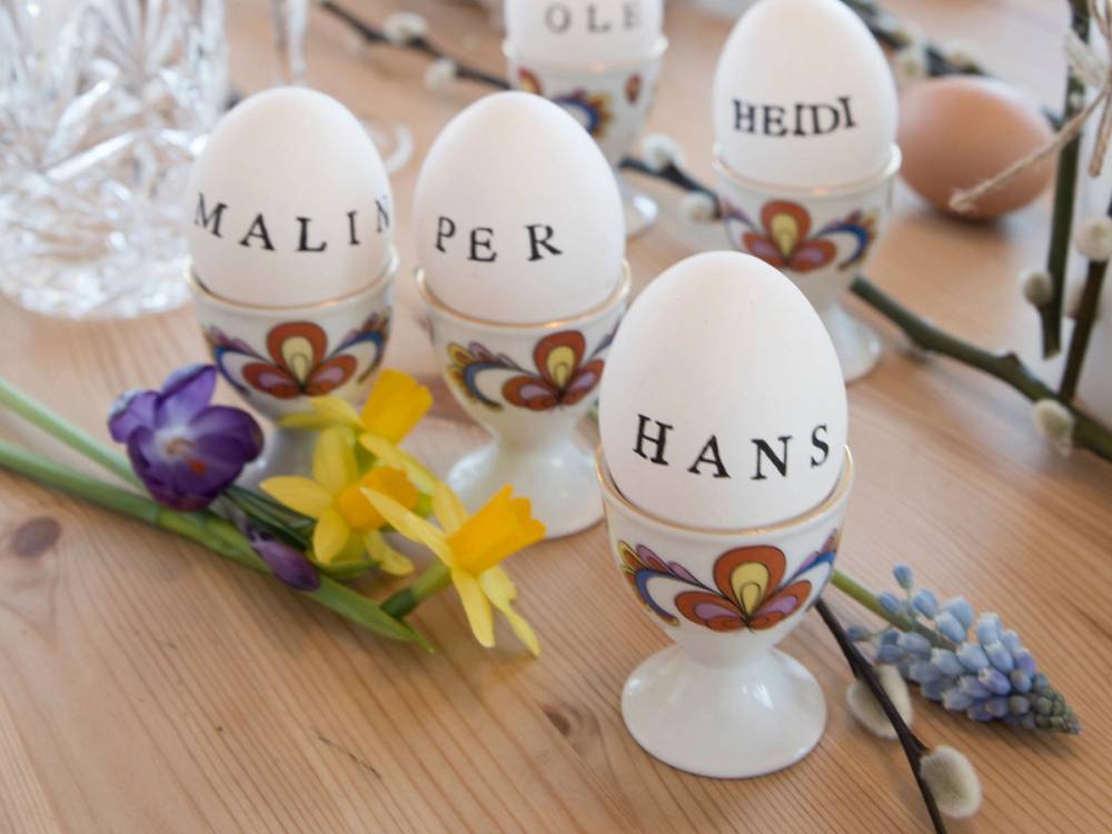 Fire påskepyntede egg med navnene Malin, Per, Hans og Heidi skrevet på dem, dekorert med blomster og påskegult bånd