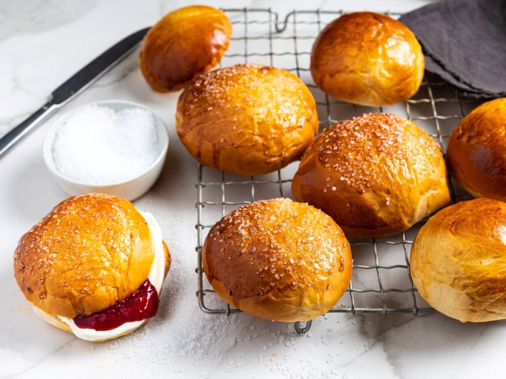 Ferske, gylne hveteboller med sukker på toppen ligger på en avkjølingsrist, med en liten skål med mel ved siden av.