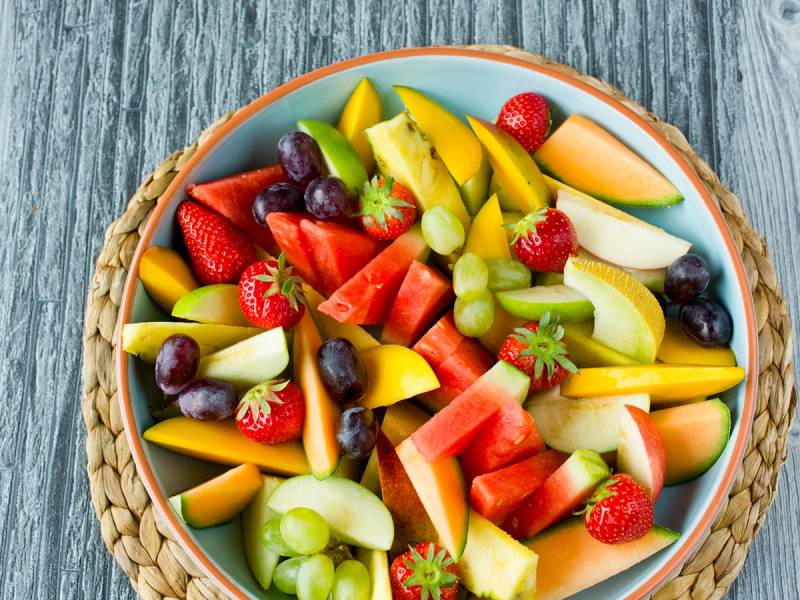 Et fat med et utvalg av fersk frukt som jordbær, druer, melon, vannmelon, kiwi og ananas på et blått fat.