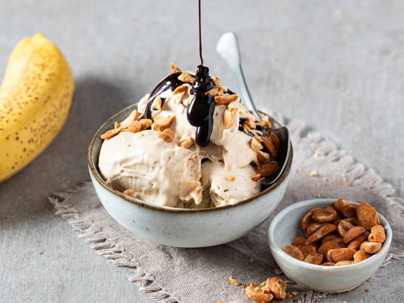 Bananis med peanøtter og sjokoladesaus i en bolle, med en liten skål med peanøtter ved siden av.