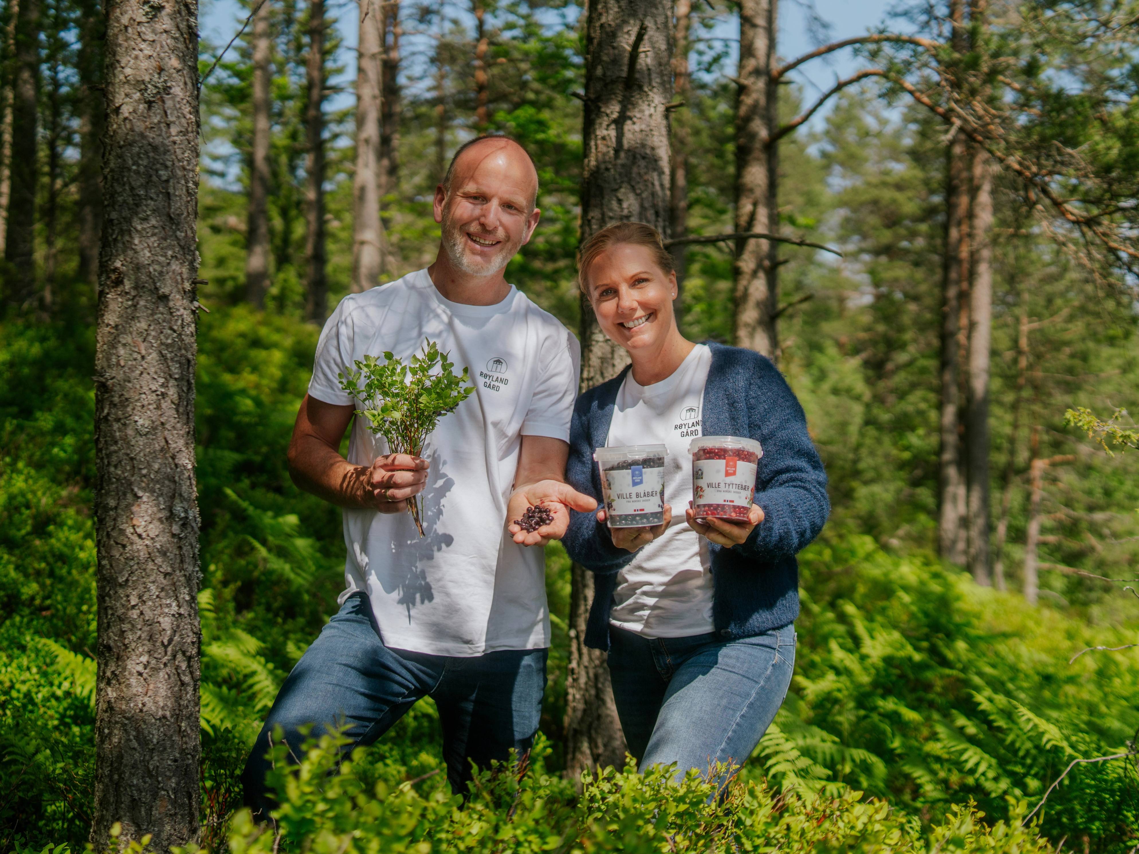 To personer i skog, en holder en plante og den andre viser pakker med jord eller frø, uten å vise ansiktene tydelig.