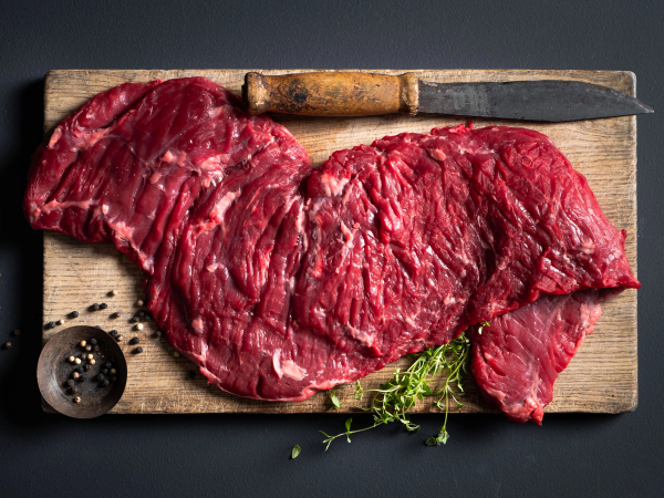 Utsnitt av rå Angus storfekjøtt på skjærebrett med kniv og krydderpepper, klar til å bli tilberedt.