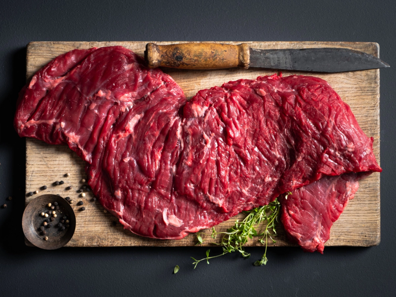 Utsnitt av rå Angus storfekjøtt på skjærebrett med kniv og krydderpepper, klar til å bli tilberedt.