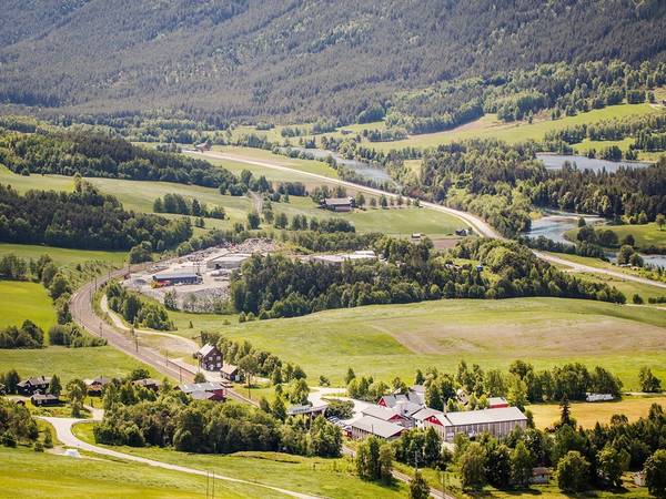Utsikt over grønne åkre og fjell i Dovre-området med spredte bygninger og veier.