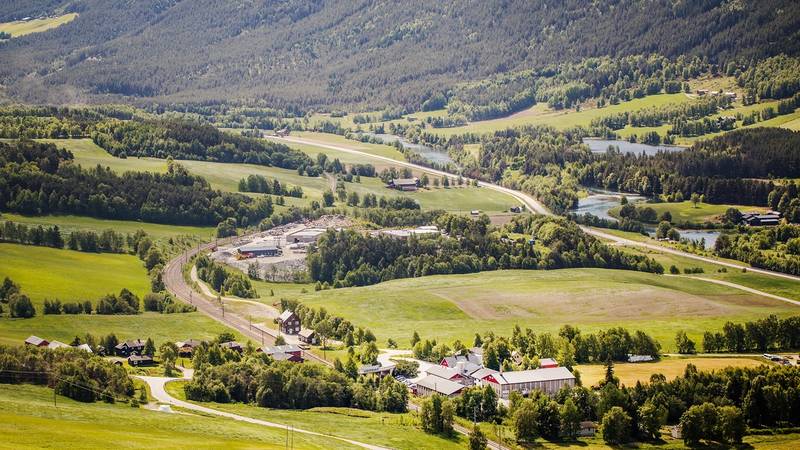Utsikt over grønne åkre og fjell i Dovre-området med spredte bygninger og veier.