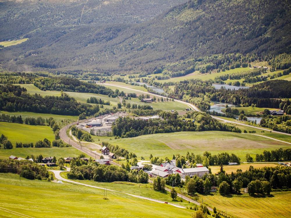 Utsikt over grønne åkre og fjell i Dovre-området med spredte bygninger og veier.