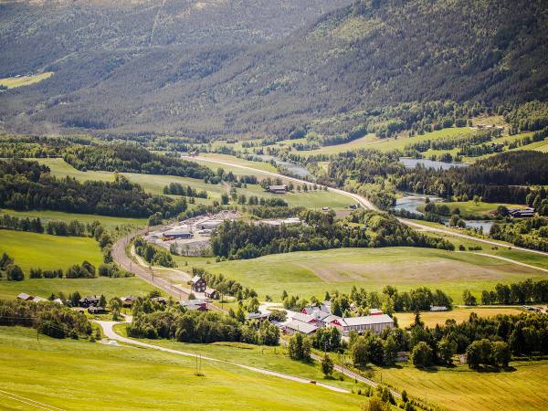 Utsikt over grønne åkre og fjell i Dovre-området med spredte bygninger og veier.
