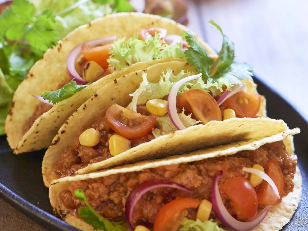 To tacos fylt med kjøttdeig, tomater, løk, mais og salat i myke tortillalefser på en tallerken.