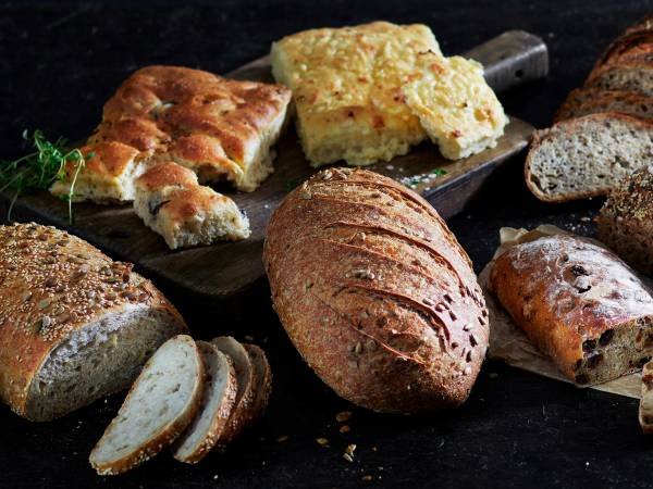 Ulike typer håndverksbrød på en svart bakgrunn, inkludert et lyst brød med sprekker, et mørkt rugbrød og et lyst brød med frø på toppen.